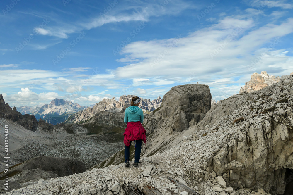 A woman hiking in high and desolated mountains in Italian Dolomites. She walks along the mountain rim and enjoys the idyllic landscape. Raw and unspoiled landscape. Sunny day. Endless mountain chains