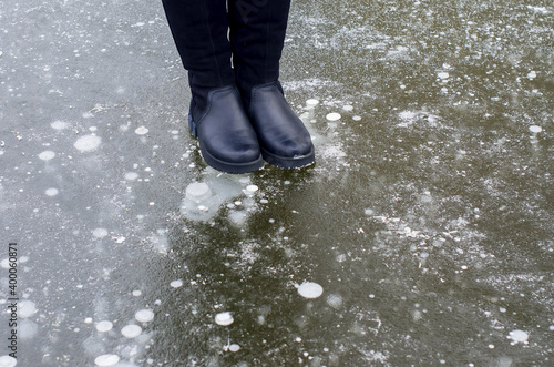 Female legs in black boots carefully walking on slippery road with frozen puddle covered with ice or thin ice of a pond. Concept of injury risk in winter and danger Dangerously slippery for pedestrian