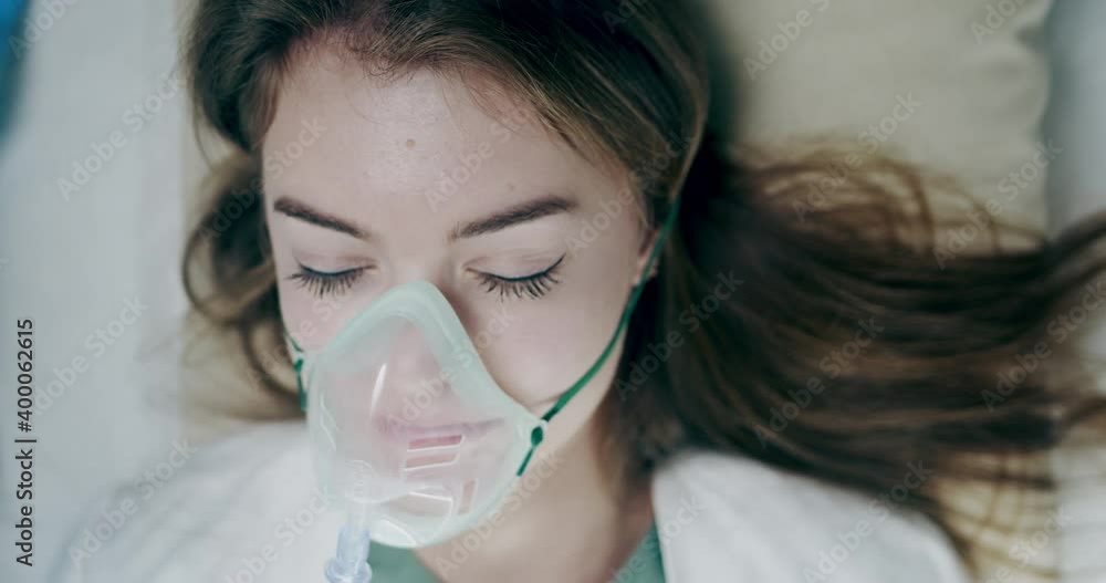 Seriously sick injured young woman nurse in oxygen mask is carried on stretcher bed to operating theatre. Emergency case.