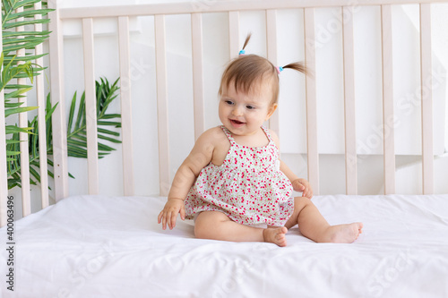 a little girl sits in a bright room in a crib and smiles