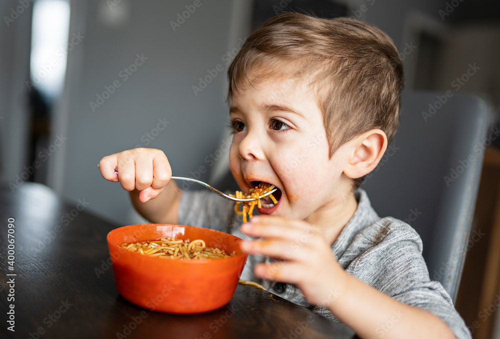 Kid eating spaghetti in the kitchen