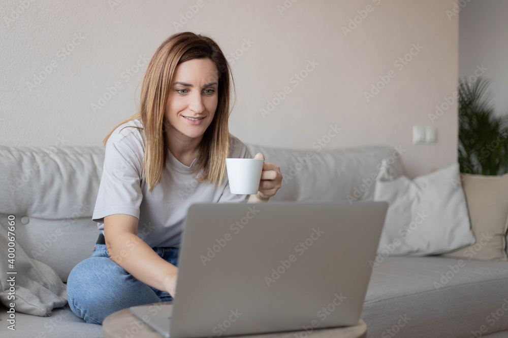 Beautiful young woman working on laptop computer while sitting at the living room, drinking coffee. Beautiful young woman working on laptop computer while sitting at the living room, drinking coffee.