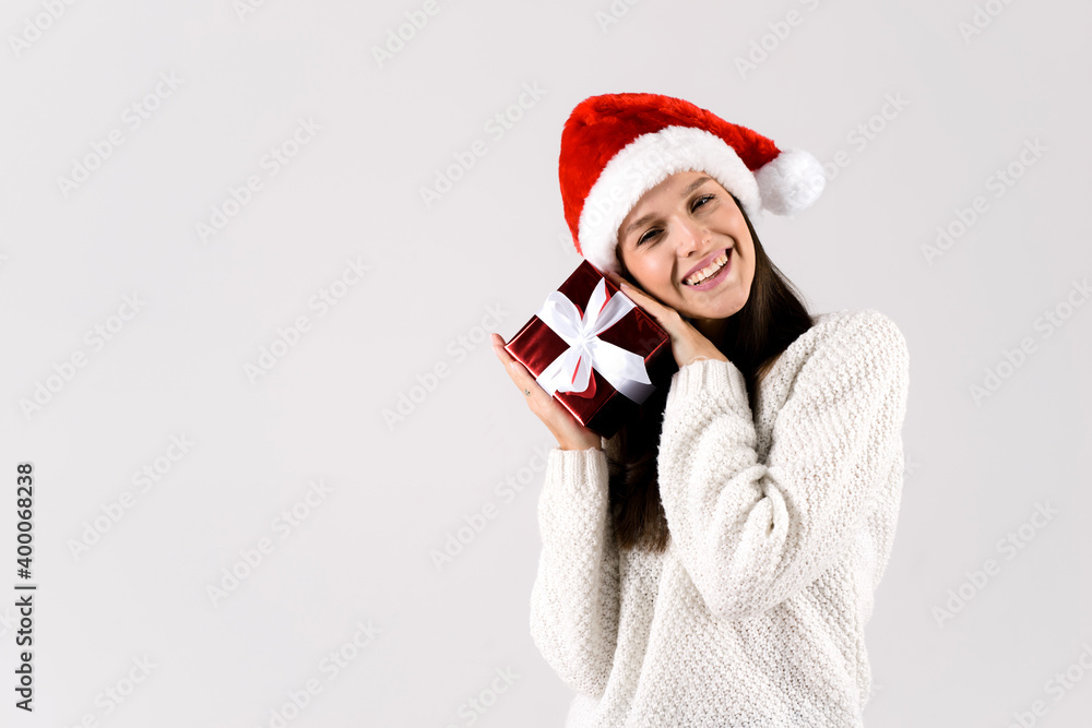 Young woman puts her ear to the gift box wrapped in red paper, isolated on white studio background Young woman puts her ear to the gift box wrapped in red paper, isolated on white studio background