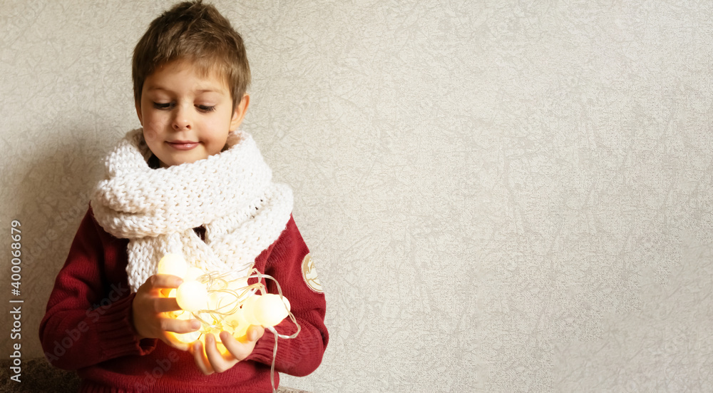 Fototapeta premium A little boy holds New Year's glowing lights in his hands. The concept of New Year and Christmas holidays, preparation for the new year. Imagination and dreams of New Year and Christmas gifts.
