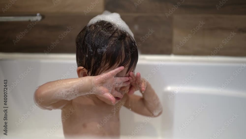 Happy two year kid bathes with toys in bath with foam Happy two year kid bathes with toys in bath with foam