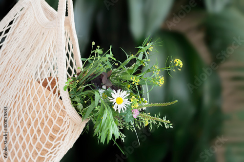 Bouquet, bunch of meadow flowers, daisies in eusable shopping eco mesh bag closeup. Romantic vacation, eco lifestyle concept. Natural background photo