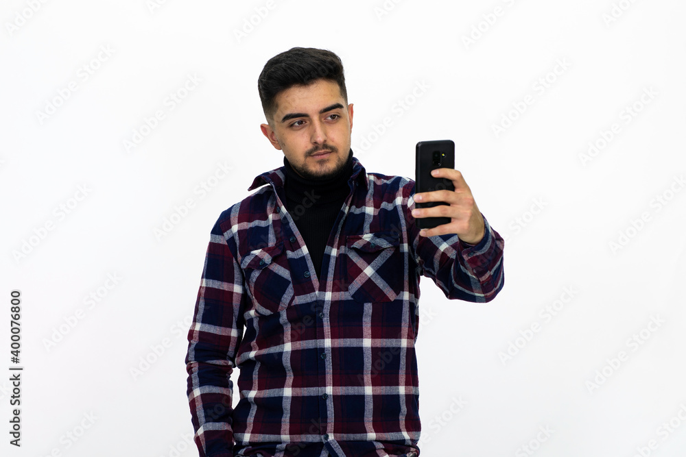 Young man wearing a dark striped shirt. He has a phone.He has a dirty beard White background. Isolated image. Young man wearing a dark striped shirt. He has a phone.He has a dirty beard White background. Isolated image.