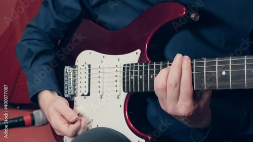 Man plays an electric guitar. Person uses vibrato, simultaneously pulls strings and turns volume and tone knobs to simulate operation of tremolo lever photo