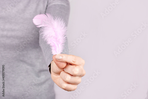 Hand with purple feather on grey background.