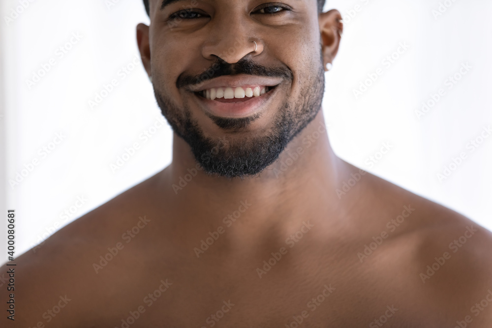 Obraz premium Close up head shot cropped image young naked african ethnicity man looking at camera, showing perfect healthy white toothy smile, satisfied with dental oral care service, feeling confident indoors.