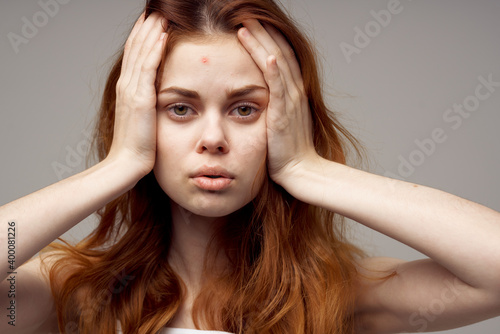 woman with loose hair touches her head with hands white t-shirt gray background