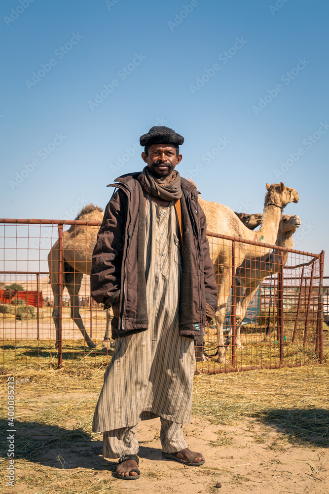 The Traditional Camel Shepherd standing in front of their camel in Al Sarar desert area -Saudi Arabia. 17-Jan-2020. The Traditional Camel Shepherd standing in front of their camel in Al Sarar desert area -Saudi Arabia. 17-Jan-2020.