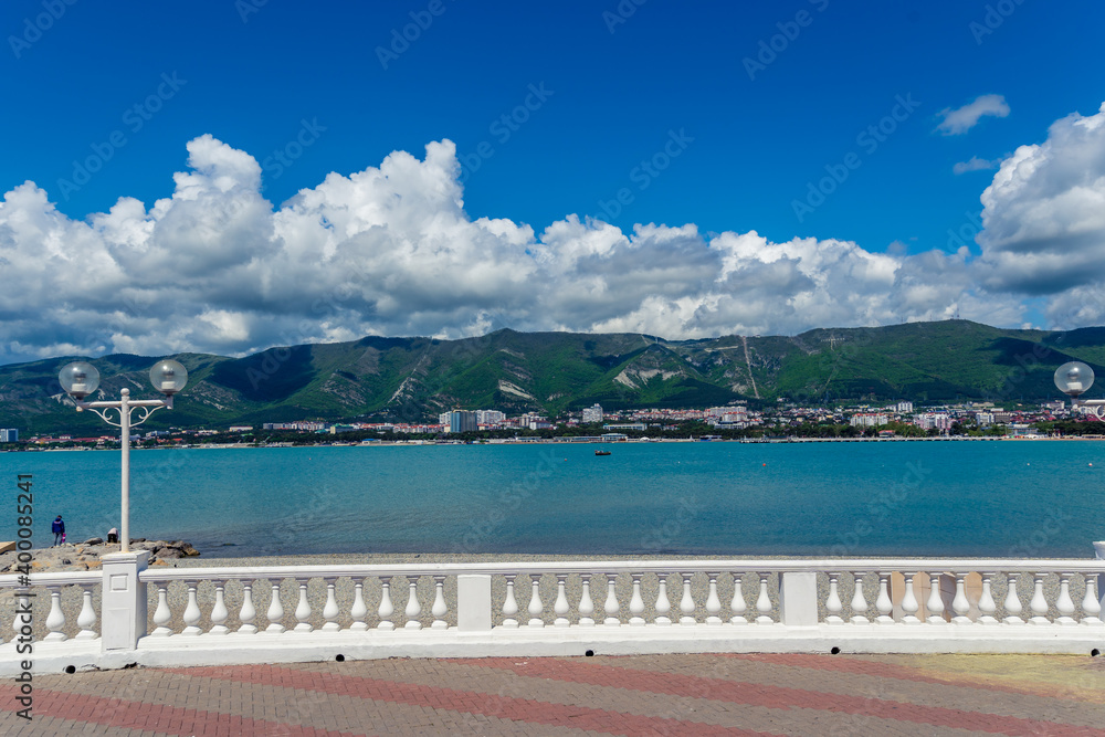 Resort embankment with balustrade and lanterns on the background of the sea and mountains. Beautiful white cumulus clouds. Seaside resort town of Gelendzhik