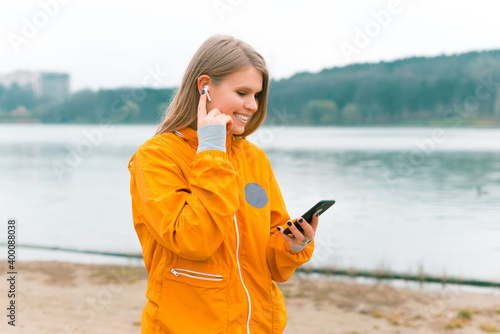 Sporty woman is walking and using her earpods and phone near a forest lake photo