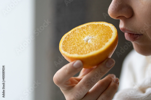 Sick woman trying to sense smell of  half fresh orange, has symptoms of Covid-19, corona virus infection - loss of smell and taste. One of the main signs of the disease.  photo