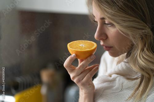 Sick woman trying to sense smell of  half fresh orange, has symptoms of Covid-19, corona virus infection - loss of smell and taste. One of the main signs of the disease.  photo