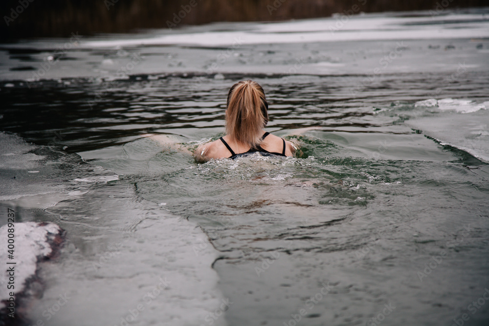 Fototapeta premium Young slender girl bathes in winter in a river hole