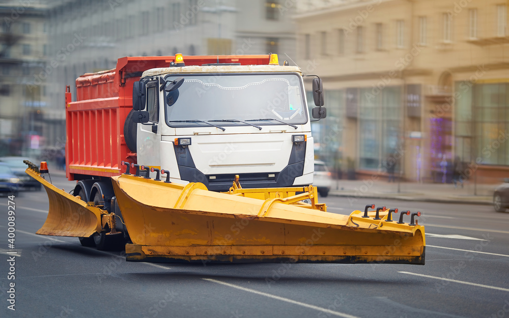 Snow plow utility truck riding on city street, municipal services preparing for winter. Tipper with plow, heavy industrial machinery for removing snow and clearing snow drifts Snow plow utility truck riding on city street, municipal services preparing for winter. Tipper with plow, heavy industrial machinery for removing snow and clearing snow drifts