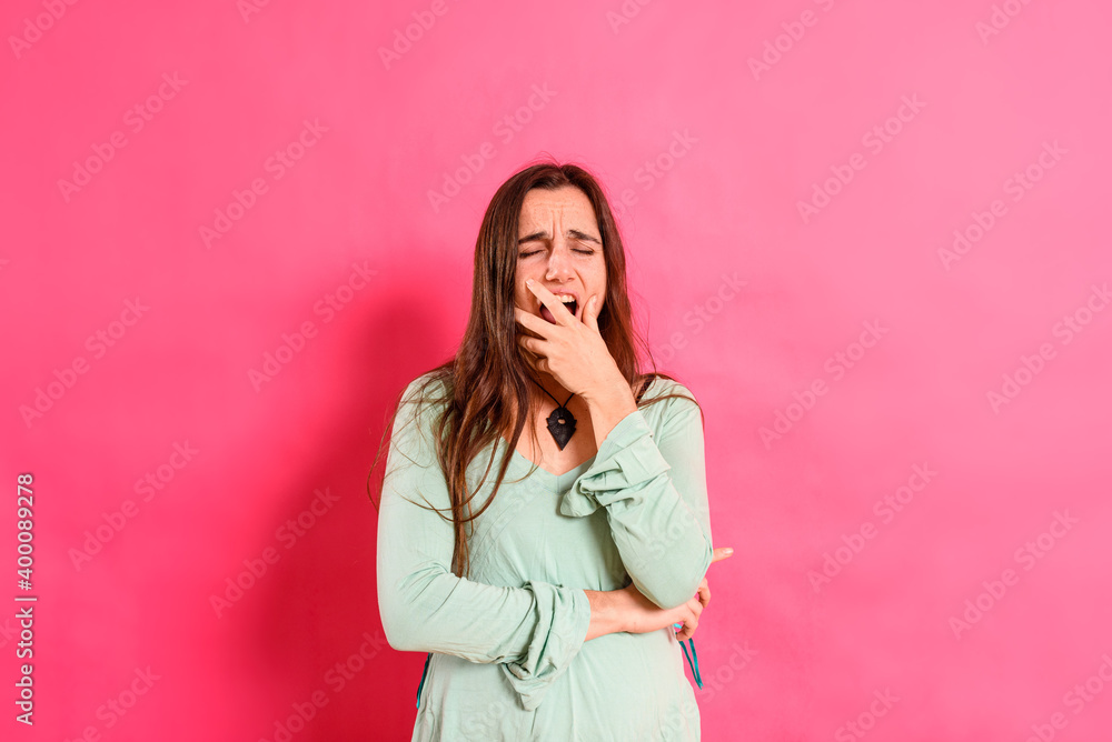 Young woman yawns from boredom and exhaustion, covering her mouth with her hand, isolated on studio background. Young woman yawns from boredom and exhaustion, covering her mouth with her hand, isolated on studio background.