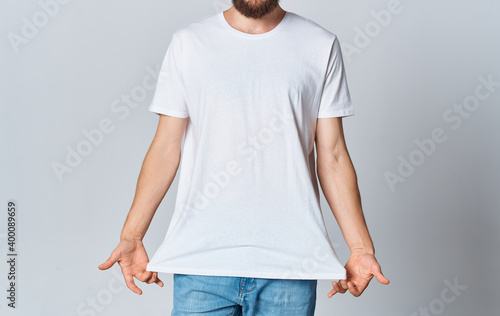 A man in a white T-shirt on a light background gestures with his hands cropped view of jeans Copy Space
