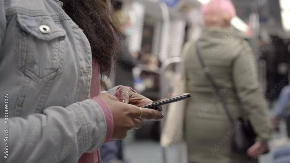 Close-up of a young African-American woman checking her phone in the subway car. Unrecognizable woman using her smart phone on public transportation. Close-up of a young African-American woman checking her phone in the subway car. Unrecognizable woman using her smart phone on public transportation.