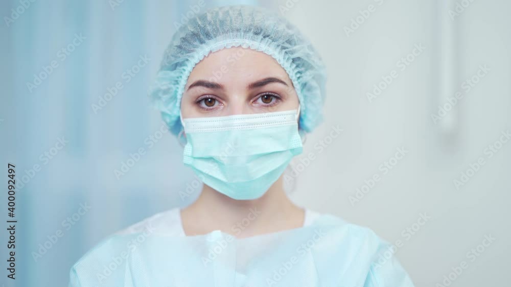 Close-up portrait of a young female doctor in a protective medical mask and hat. Hispanic woman looking at the camera on a light white background in a hospital room. Portrait of an ambulance nurse Close-up portrait of a young female doctor in a protective medical mask and hat. Hispanic woman looking at the camera on a light white background in a hospital room. Portrait of an ambulance nurse