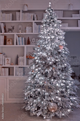 flocked illuminated christmas tree in front of the bookcase, cozy home interior