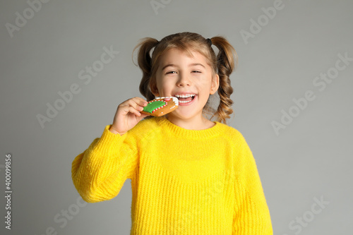 Cute little girl with Christmas gingerbread cookie on light grey background
