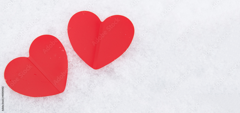 Two beautiful romantic red hearts together on a white snowy background. The concept of love and Valentine's Day