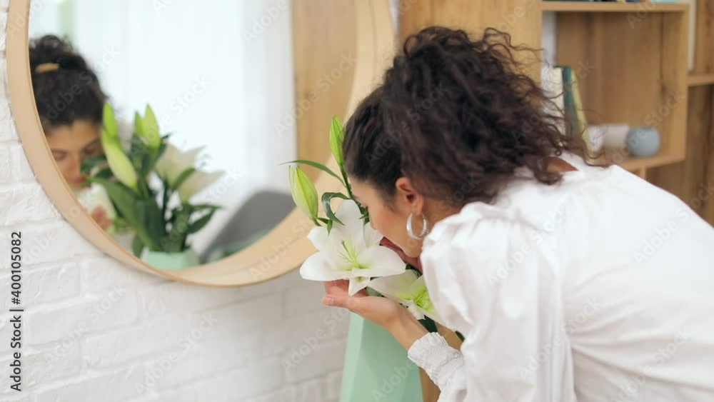 Young woman sniffing bouquet of beautiful lilies in vase Young woman sniffing bouquet of beautiful lilies in vase