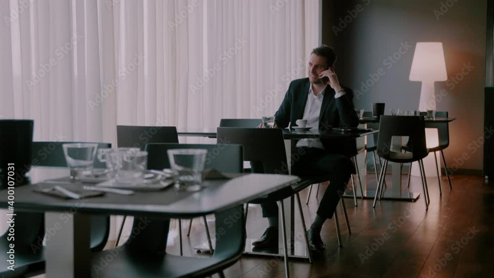 Businessman sitting at an empty table and smiling while talking on the phone Businessman sitting at an empty table and smiling while talking on the phone