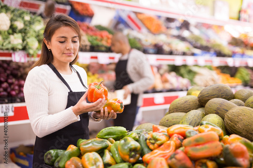 Supermarket woman worker in black apron putting vegetables in her department