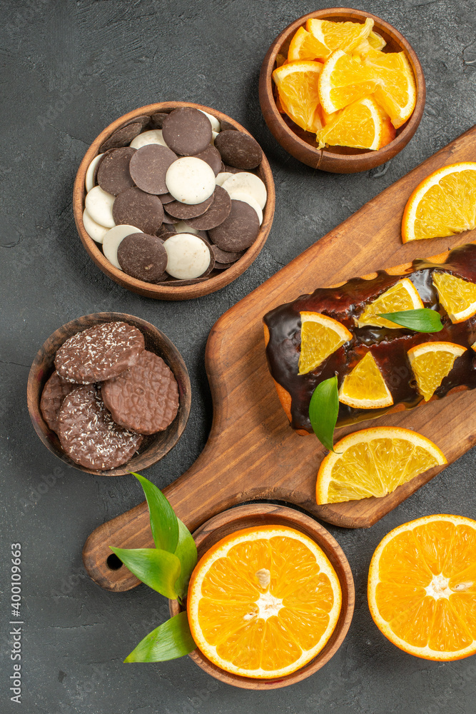 Soft cakes on wooden cutting board and cut lemons with leaves biscuits on dark background Soft cakes on wooden cutting board and cut lemons with leaves biscuits on dark background