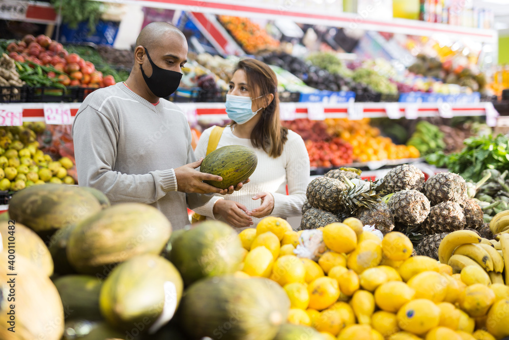 Husband and wife wearing protective masks picking ripe melon at a grocery supermarket