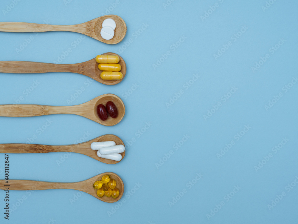 Dietary supplements and vitamins on wooden spoons on a blue background with space for text, top view, flat lay. The concept of a healthy lifestyle, taking care of your health. Vitamin b, c, e, zinc Dietary supplements and vitamins on wooden spoons on a blue background with space for text, top view, flat lay. The concept of a healthy lifestyle, taking care of your health. Vitamin b, c, e, zinc