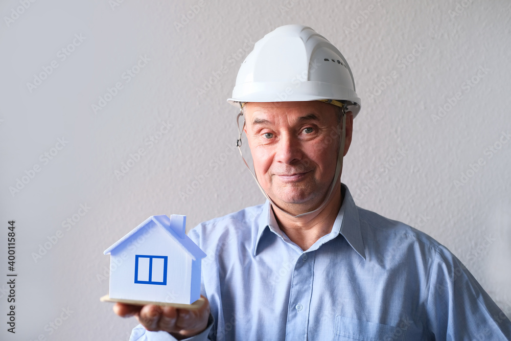 elderly male agent, a builder in a protective helmet, glasses offers to rent, buy a house, shows a model of a house, a mortgage concept, advice on buying a property elderly male agent, a builder in a protective helmet, glasses offers to rent, buy a house, shows a model of a house, a mortgage concept, advice on buying a property