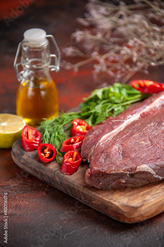 Side view of red meat on wooden cutting board and garlic green chopped pepper oil bottle lemon on dark background