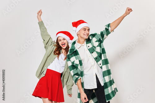 Happy loving couple gestures with their hands on a light background and a Christmas hat on their heads