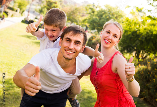 young family of three having fun in park on summer day and holding thumbs up .