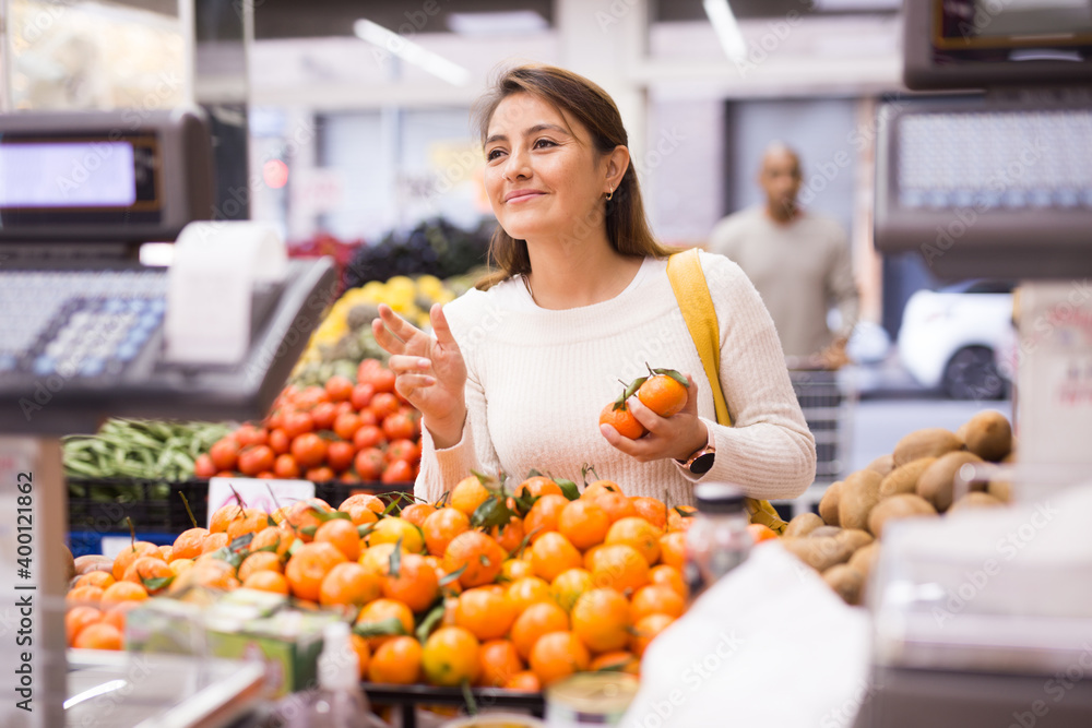 Female shopper selects ripe tangerines in a grocery hypermarket