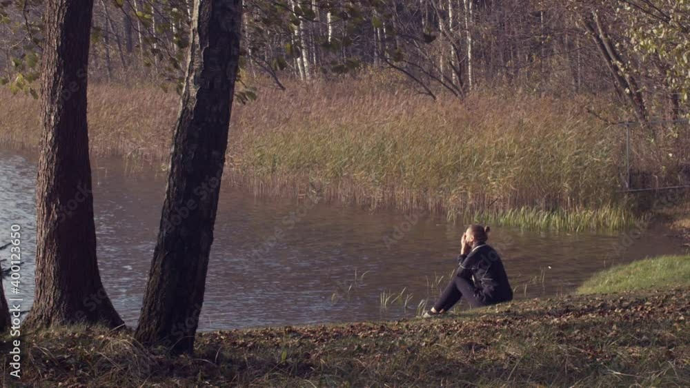 Lonely girl sitting at lakeside outdoors thinking of life slow motion natural daylight. Portrait of pensive woman dreaming alone at lakeshore. Loneliness solitude lifestyle troubles problem solution. Lonely girl sitting at lakeside outdoors thinking of life slow motion natural daylight. Portrait of pensive woman dreaming alone at lakeshore. Loneliness solitude lifestyle troubles problem solution.