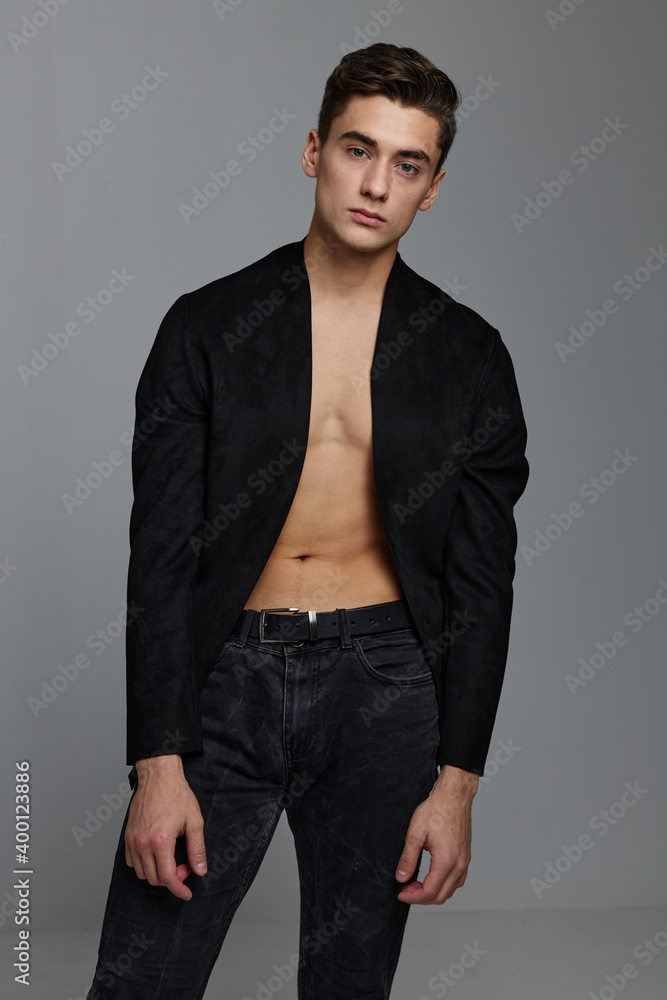 Fototapeta premium A gentleman in an unbuttoned jacket on a naked torso and in trousers on a gray background