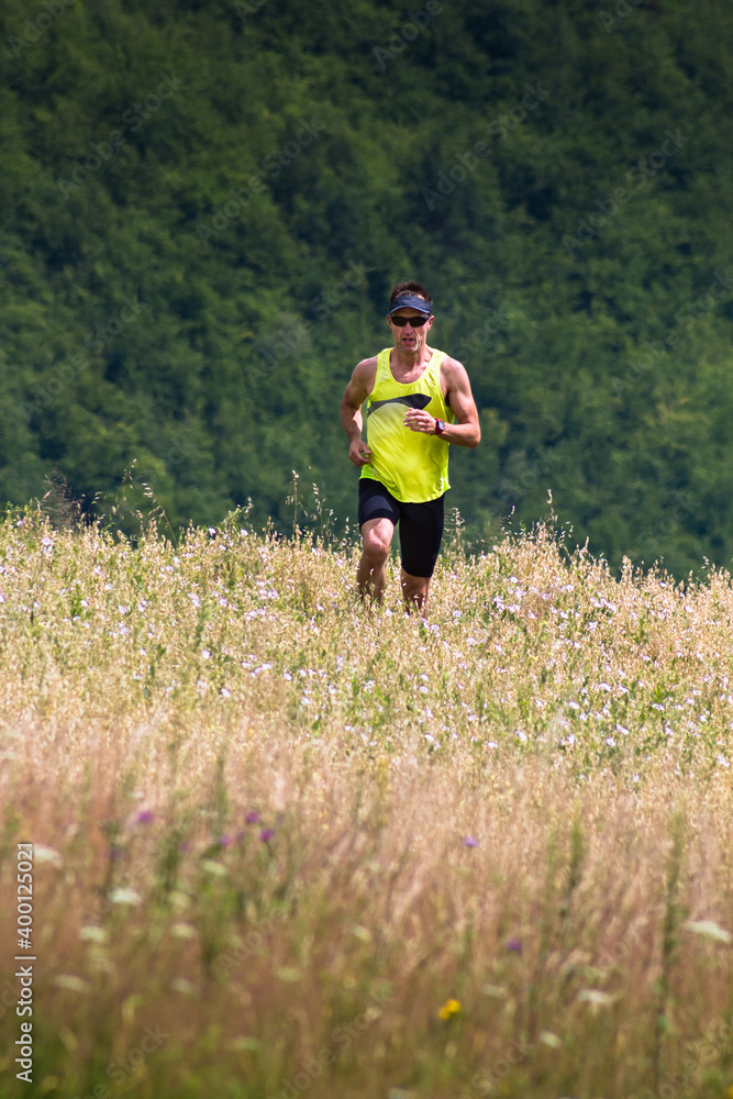 Athletic man runner running in mountains through wild grass