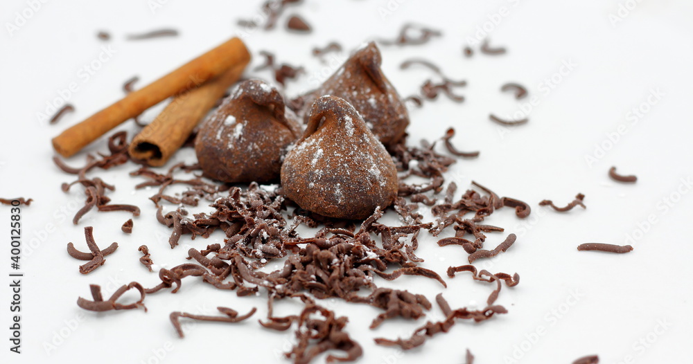 Fototapeta premium Trufas de chocolate con palitos de canela y virutas de chocolate sobre fondo blanco.