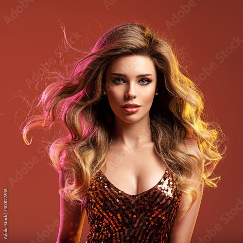 Portrait of beautiful young woman with bright shiny makeup. Blonde with brightly colored long hair. Pretty girl with long curly hair. Fashion model in a shiny dress posing at studio.