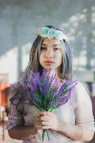 Portrait close up of young beautiful Asian women Beautiful girl in the pink dress with purple flowers  in hands on a light background. Woman day.