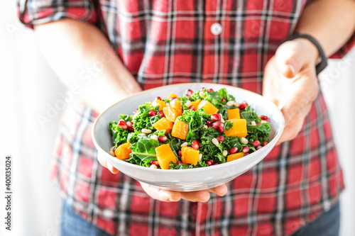 Vegetable salad bowl in woman hands. Fresh kale and baked pumpkin salad. Healthy eating concept