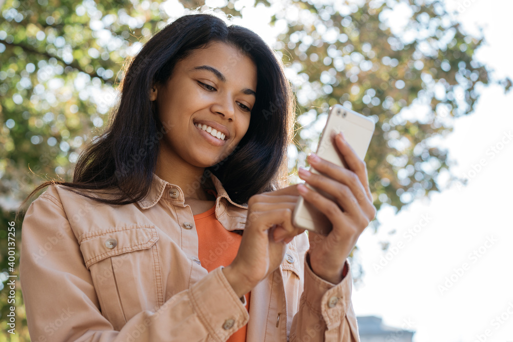 Beautiful African American woman using mobile app for online shopping. Young smiling female holding smartphone, chatting, communication, looking at digital screen Beautiful African American woman using mobile app for online shopping. Young smiling female holding smartphone, chatting, communication, looking at digital screen