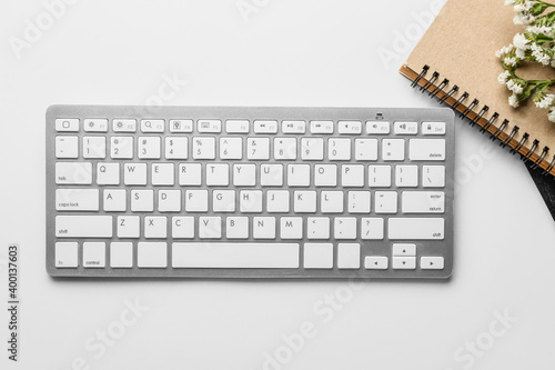 Computer keyboard, notebooks and flowers on light background