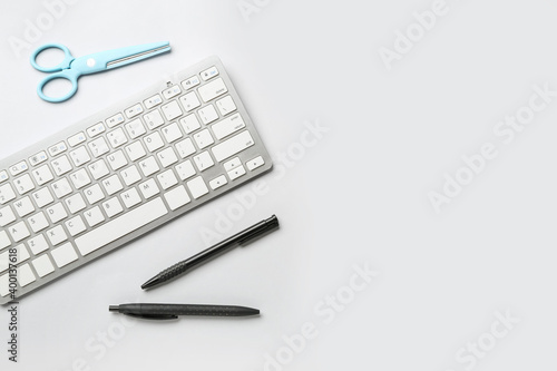 Computer keyboard, pens and scissors on white background